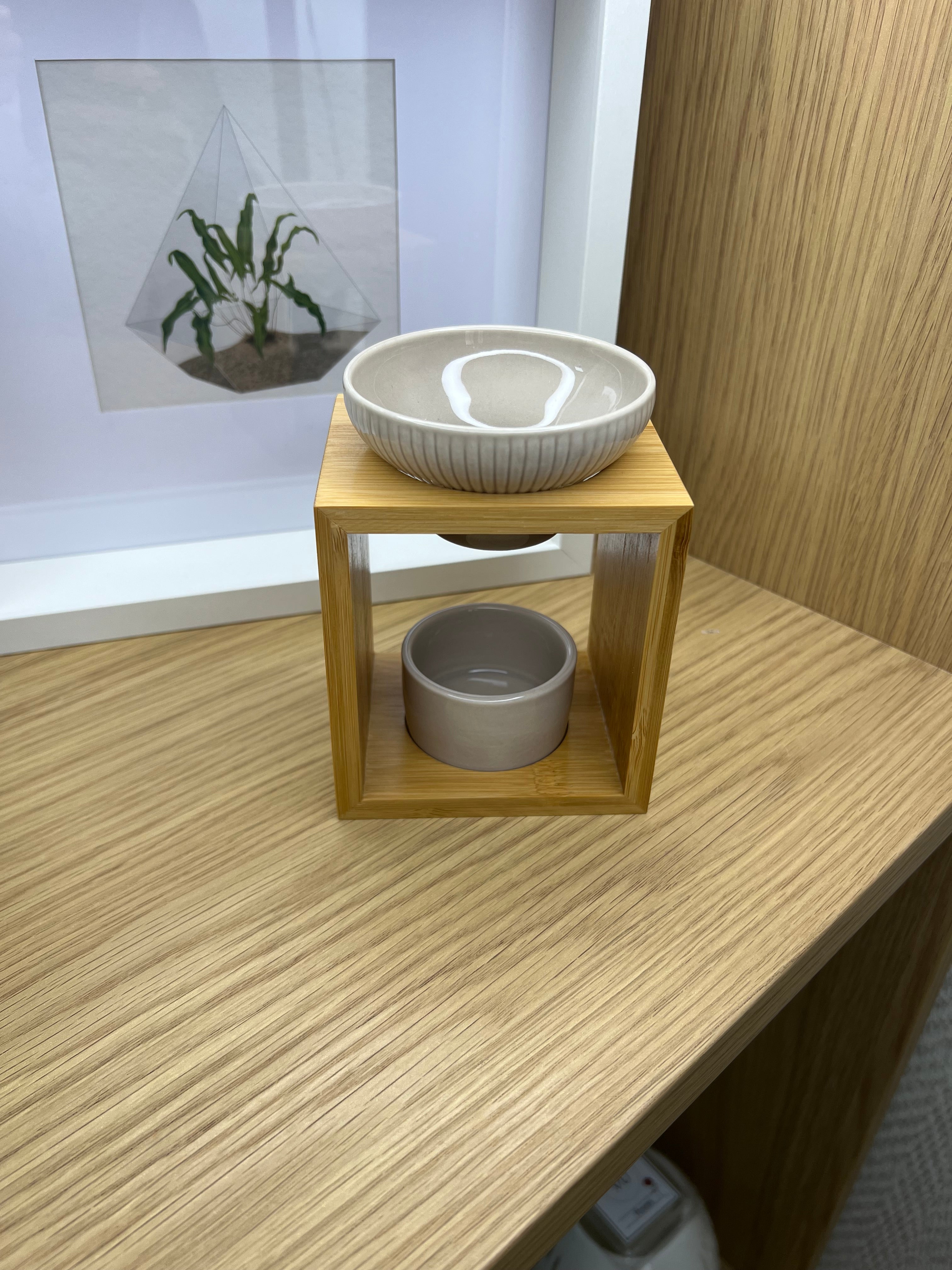 Quemador de cera artesanal con estructura de madera natural y cuenco superior de cerámica blanca acanalada.